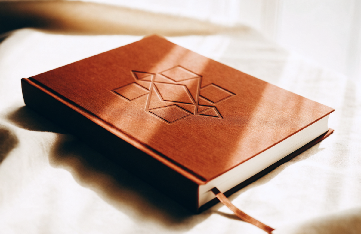 The Book About a child — a terracotta cloth hardcover, gold-embossed with a geometric rosette, resting on cream linen